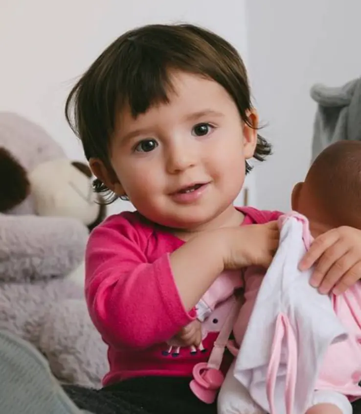 طفلة صغيرة تبتسم وهي تحمل دميتها.